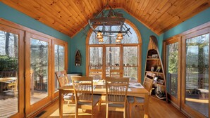A cozy cabin interior with a wooden dining table and chairs, large windows offering a view of the forest, and a unique ceiling design. - Pet-Friendly,Cedar Cabin, Spa Tub, WiFi,Fireplace (Ferguson)