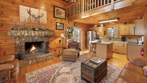 A cozy cabin interior with a stone fireplace, leather furniture, a kitchen with wooden cabinets, and a loft bedroom. - Pet-Friendly,Cedar Cabin, Spa Tub, WiFi,Fireplace (Ferguson)