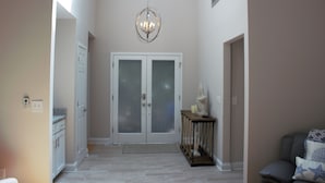 Ein Flur mit einer Doppeltür, einer Chandelier, einem kleinen Tisch mit Dekoration und einer Bank mit Kissen.