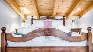 Una cama con estructura de madera, cabecera, ropa de cama blanca y almohada rosa.