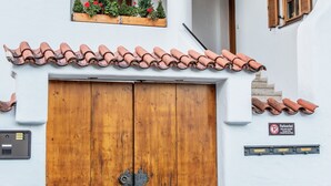 Un edificio con puerta de madera, tejado de tejas y una ventana pequeña con plantas.