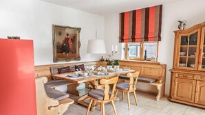 Un comedor con mesa de madera, sillas y bancos. Hay un armario con puertas de cristal y un cuadro en la pared.