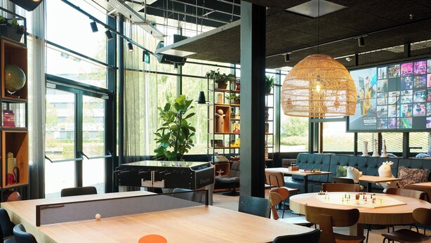 Un espace intérieur moderne doté d’une table de ping-pong, de coins salon et de grandes fenêtres.