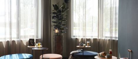 A room with a large window, a potted plant, a small table with a cup, a bench, and a suitcase against the wall.