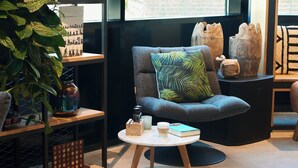 Un coin salon confortable avec un fauteuil moelleux, une petite table ronde agrémentée d’une bougie et d’un livre, et une grande plante.