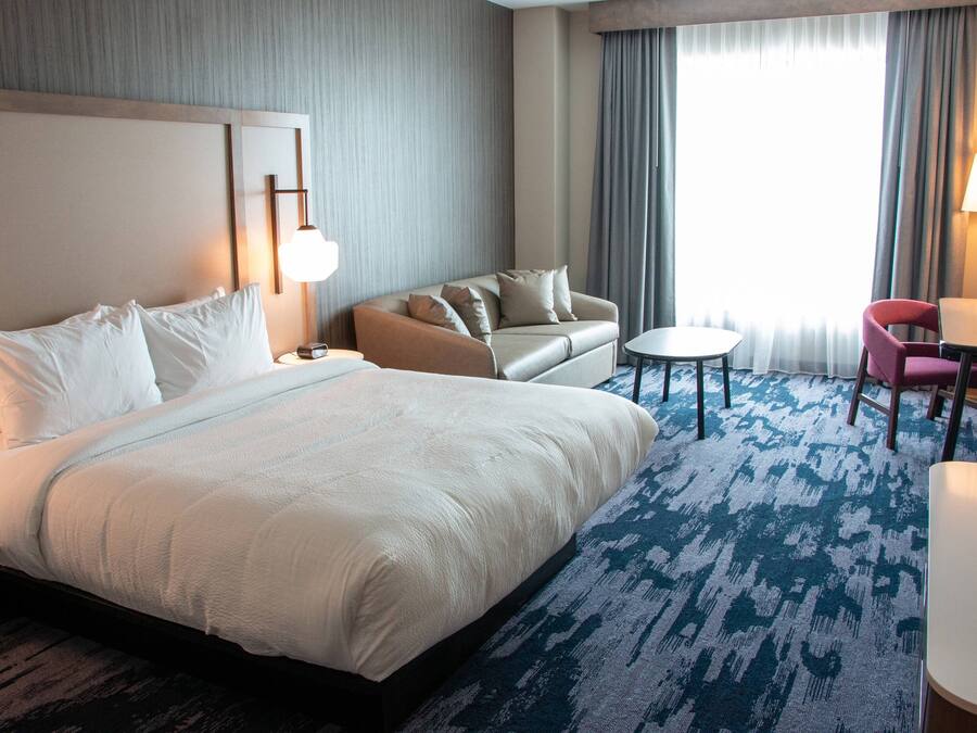 A hotel room with a large bed, a sofa, a small table, and a chair.