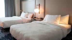 Hotelkamer met twee bedden, een nachtkastje met een telefoon en afstandsbediening, en een wandlamp.