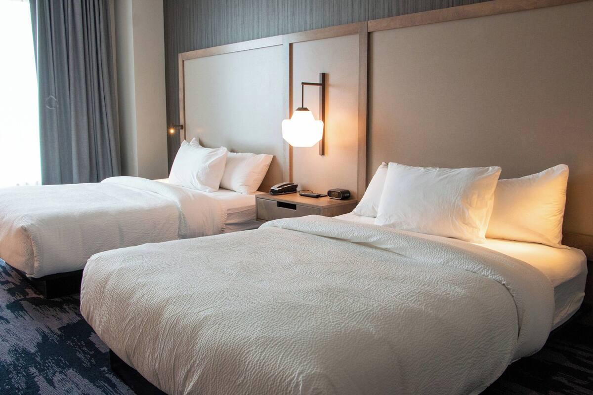 Hotelkamer met twee bedden, een nachtkastje met een telefoon en afstandsbediening, en een wandlamp.