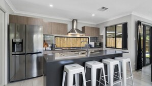 A modern kitchen with stainless steel appliances, a central island with bar stools, and a large window providing a view of the outdoors. - FAMILY BEACH HOLIDAY HOUSE (WOORIM)