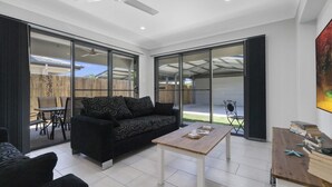 A modern living room with a black sofa, a wooden coffee table, and a dining area with a table and chairs. Large glass doors lead to an outdoor patio. - FAMILY BEACH HOLIDAY HOUSE (WOORIM)