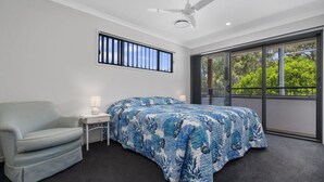 A bedroom with a bed, a chair, a nightstand, a ceiling fan, a window with a view of trees, and a balcony. - FAMILY BEACH HOLIDAY HOUSE (WOORIM)