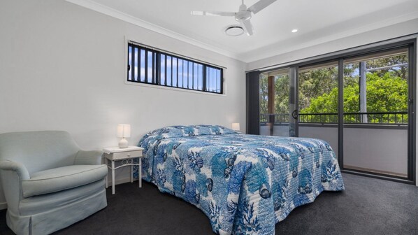 A bedroom with a bed, a chair, a nightstand, a ceiling fan, a window with a view of trees, and a balcony. - FAMILY BEACH HOLIDAY HOUSE (WOORIM)