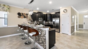 A modern kitchen with a central island, bar stools, stainless steel appliances, and a decorative wall piece. - 1433rf- The Retreat at Championsgate (Davenport)