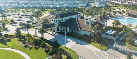 A residential area with a large house featuring a swimming pool, surrounded by well-maintained lawns and palm trees.