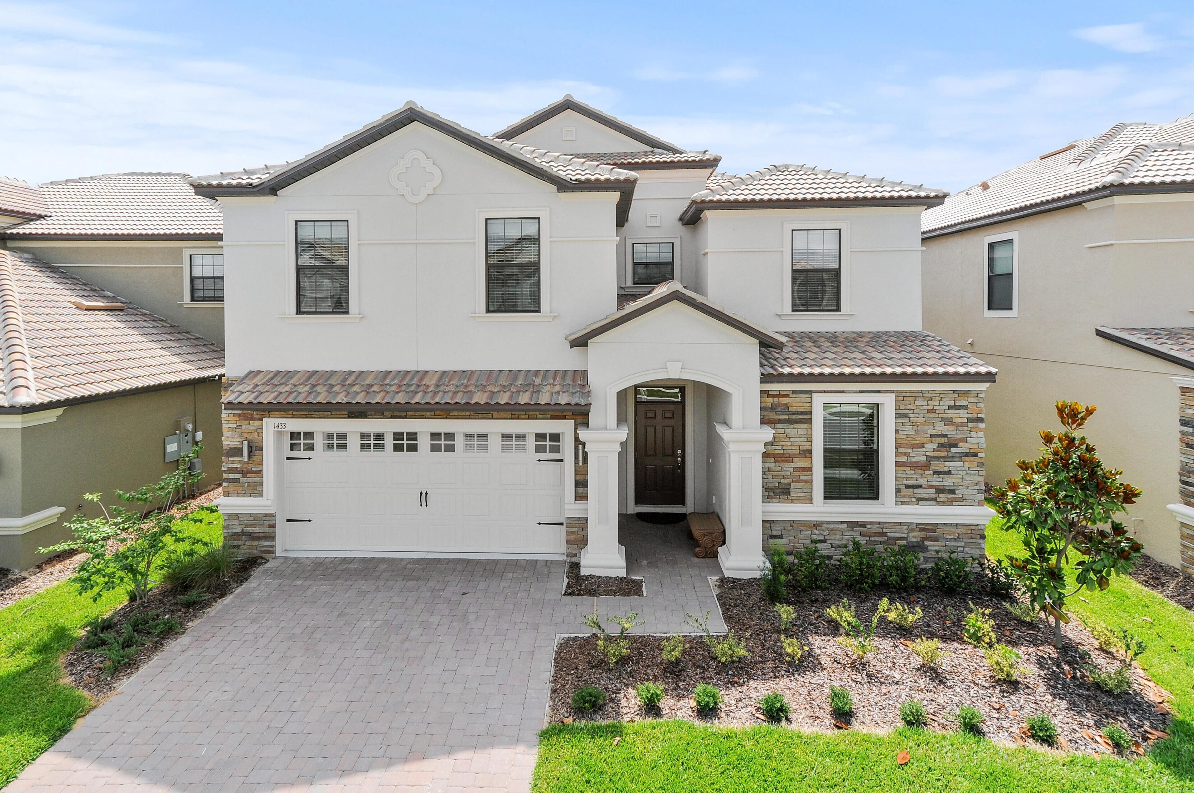 A two-story house with a white garage door, a stone facade, and a tiled roof.
