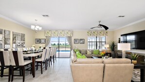 A spacious living room with a large sofa, dining area with chairs, and a TV. - 1433rf- The Retreat at Championsgate (Davenport)