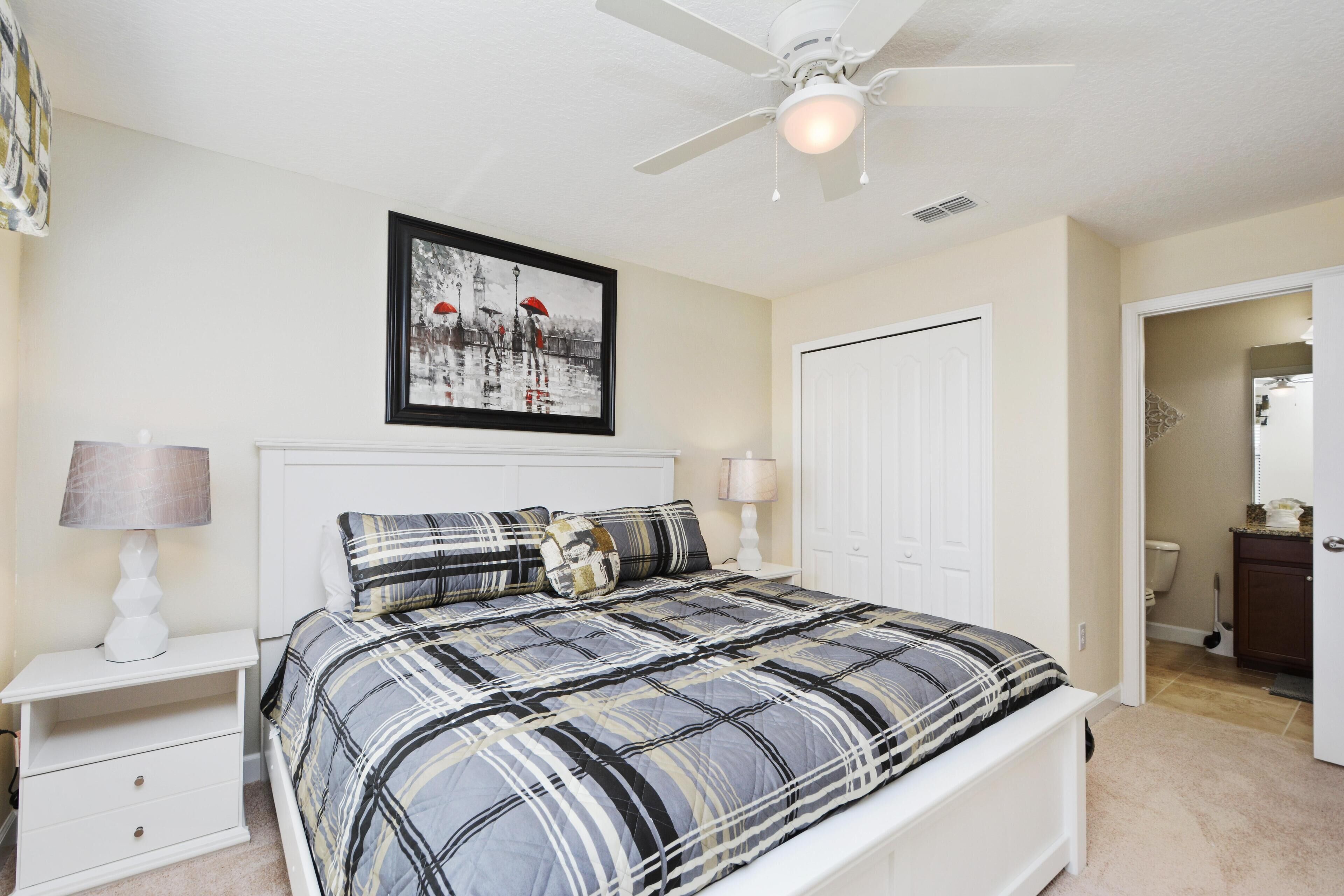 A bedroom with a bed, nightstands, a ceiling fan, a framed picture, and a door.