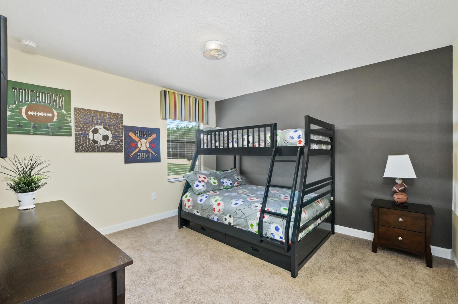 Una cama litera con edredón de temática futbolística, una mesita de noche con lámpara y decoración de pared con motivos deportivos.