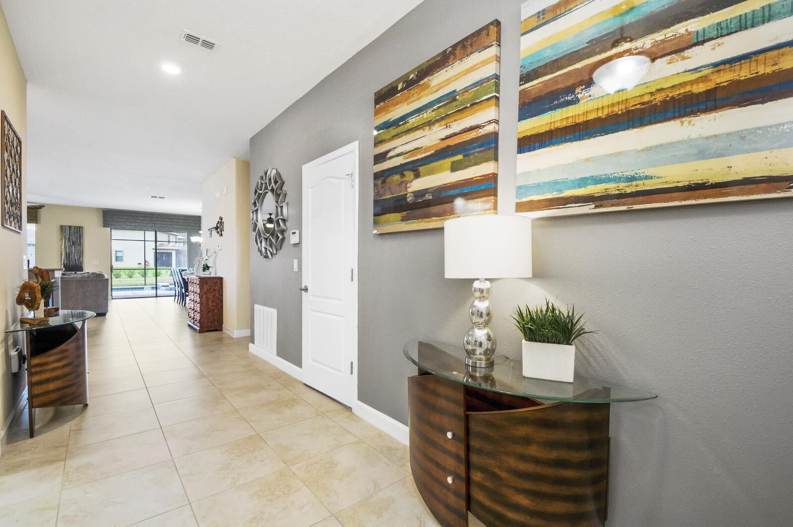 A hallway with a glass-top console table, a potted plant, and a decorative mirror.