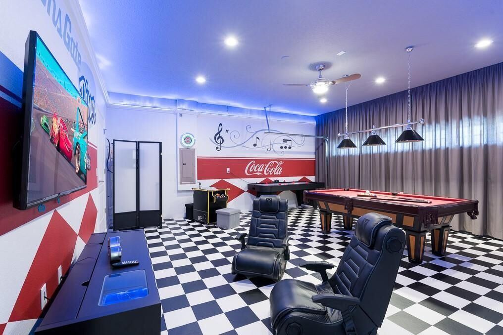 A room with a pool table, pool chairs, a television, and a Coca-Cola mural.
