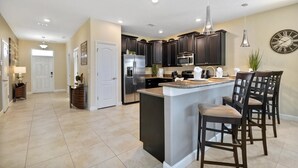 A modern kitchen with dark cabinets, stainless steel appliances, and a central island with bar stools. - 1461rf - NON Renting 1/5/2022 The Retreat at Championsgate (Davenport)
