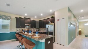 A modern kitchen with dark cabinets, a central island with bar stools, stainless steel appliances, and a teal accent wall. - 1542mvd-the Retreat at Champions Gate (Davenport)