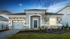 A two-story house with a stone facade, a garage, and a well-maintained lawn. - 1542mvd-the Retreat at Champions Gate (Davenport)