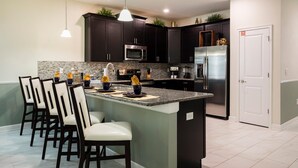 Una cocina moderna con armarios oscuros, electrodomésticos de acero inoxidable y una isla central con taburetes de bar.