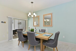 A dining area with a wooden table, six grey upholstered chairs, a chandelier, and framed artwork on the walls. - 1588sw-the Retreat at Championsgate (Davenport)