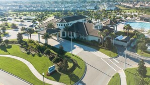 A residential area with a large house featuring a swimming pool, surrounded by well-maintained lawns and palm trees.