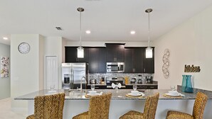 A modern kitchen with dark cabinets, stainless steel appliances, and a central island with bar-style chairs.