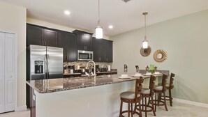 Una cocina moderna con armarios oscuros, electrodomésticos de acero inoxidable, encimera de granito y una zona de bar con taburetes.