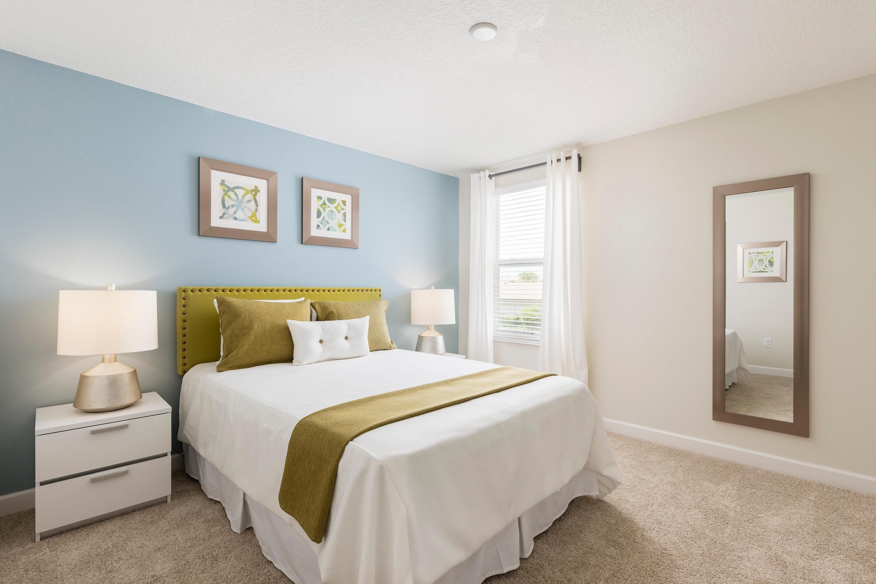 A bedroom with a bed, nightstands, a mirror, and two framed pictures on the wall.