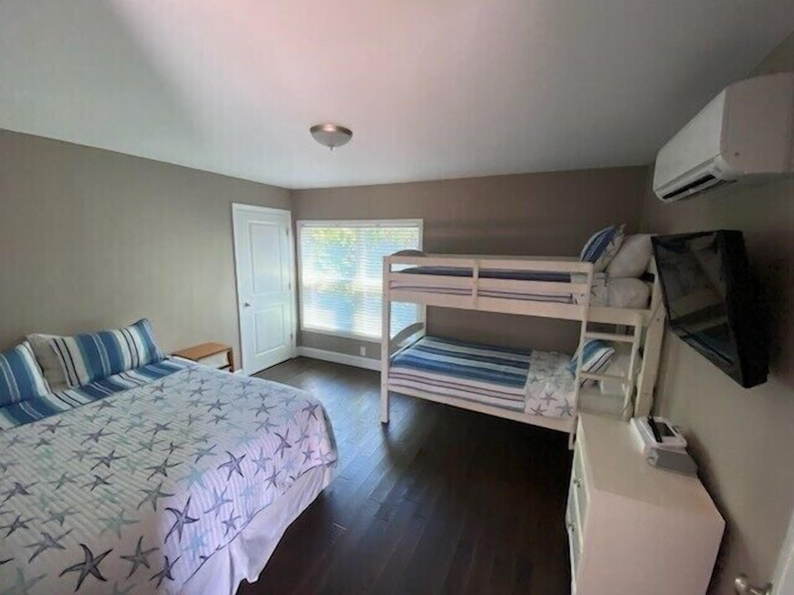 A bedroom with a bunk bed, a single bed, a desk, and an air conditioning unit.