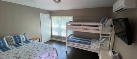 A bedroom with a bunk bed, a single bed, a desk, and an air conditioning unit.