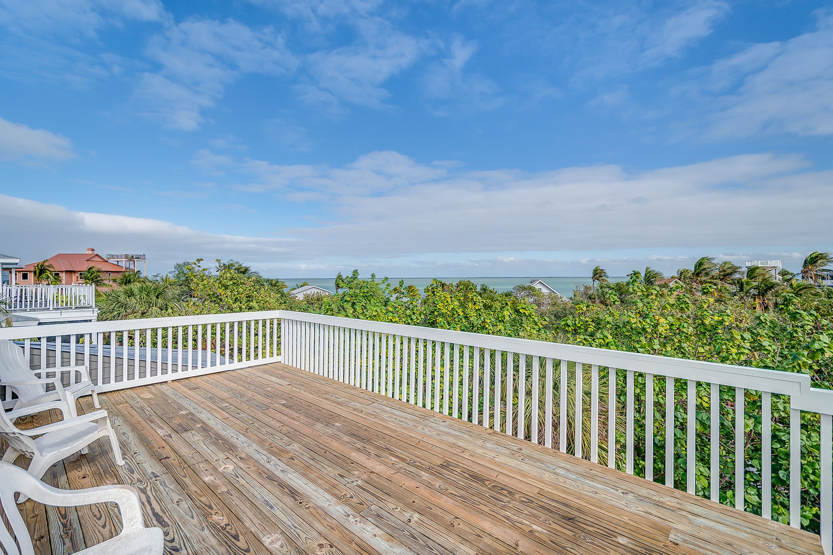 Um deck de madeira com guarda-corpos brancos, com vista para uma paisagem verde exuberante e o oceano.