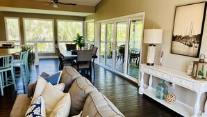 A spacious living room with a large beige sectional sofa, a dining area with a table and chairs, and a view through large glass doors to an outdoor patio. - Near beach, includes golf cart , bikes , kayaks and pool , 5 stars. NCIC member (Captiva)