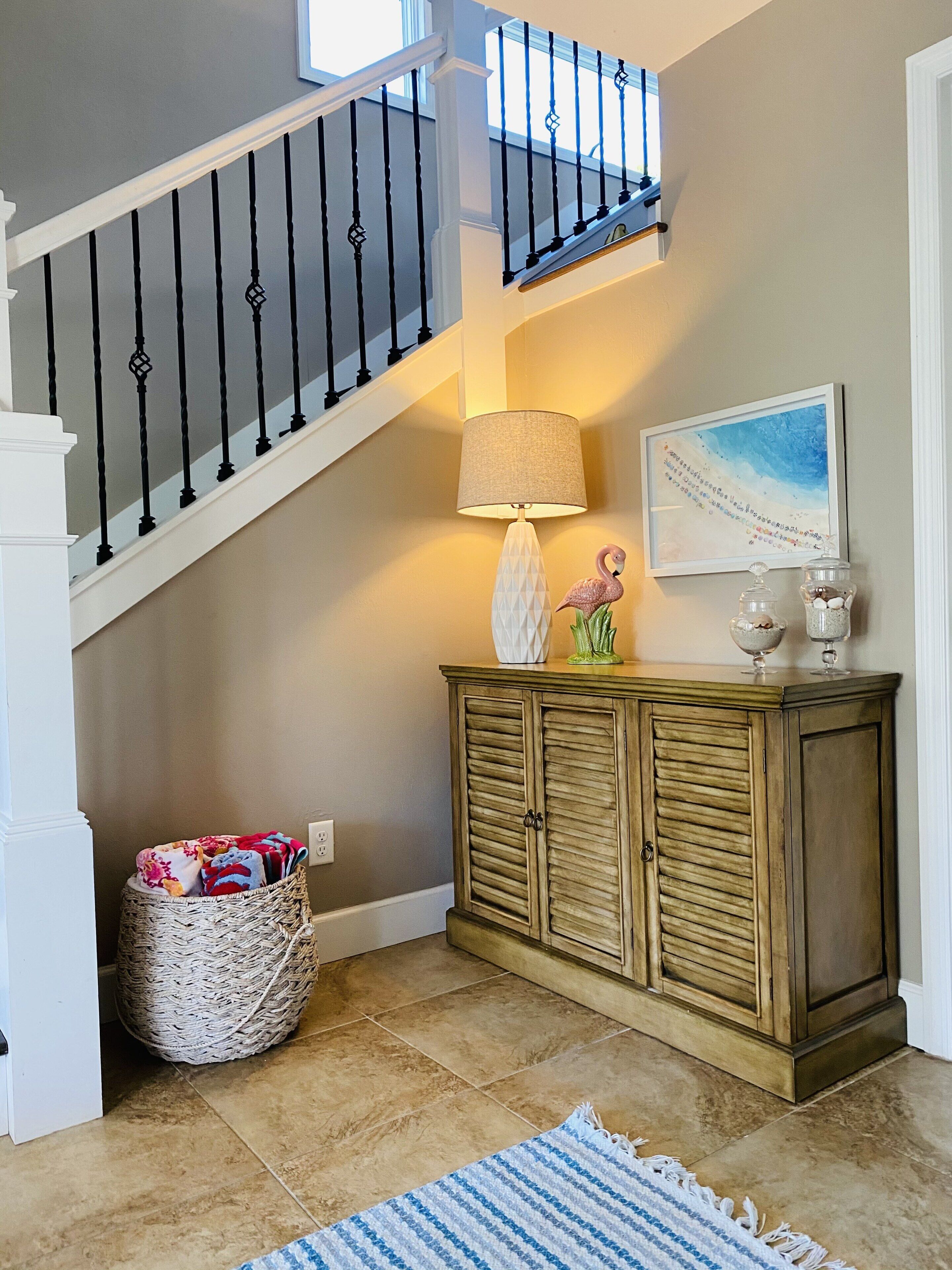 A staircase with black balusters, a wicker basket with blankets, a cabinet with decorative items, and a framed picture on the wall.