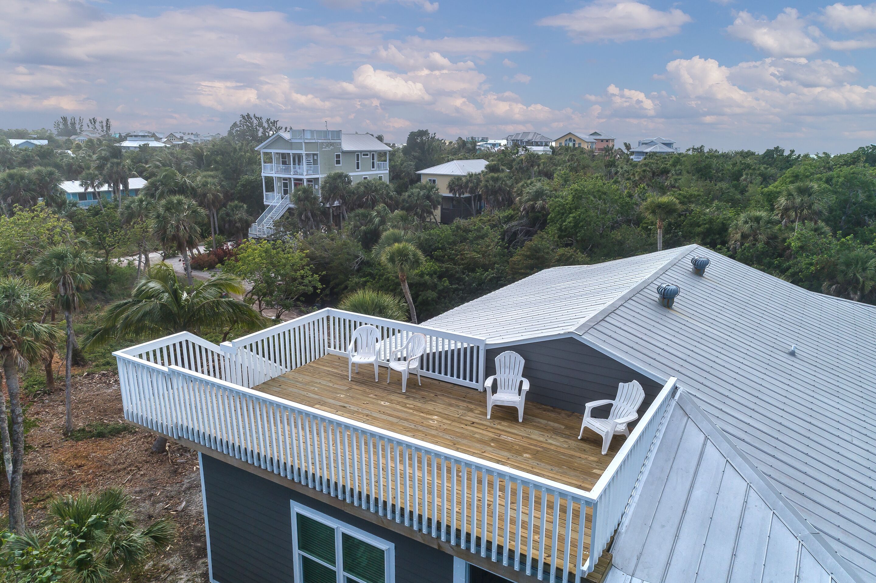 Une maison avec une terrasse en bois, des rampes blanches et plusieurs chaises Adirondack.