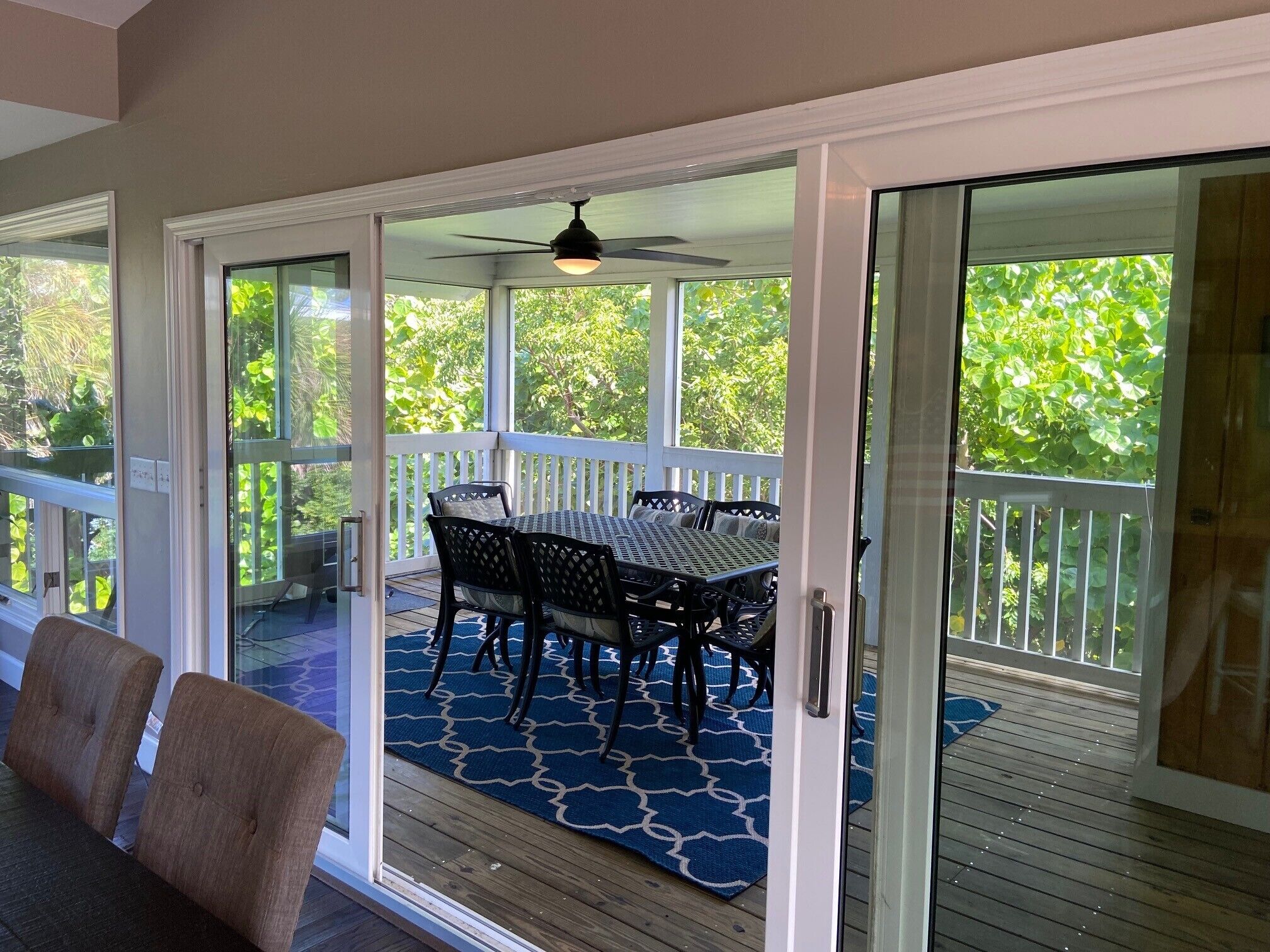 Une terrasse extérieure couverte, équipée d’une table et de chaises, d’un ventilateur de plafond et offrant une vue sur la verdure.