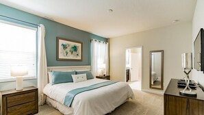 Une chambre à coucher avec un lit, des tables de chevet, une commode, un miroir et une fenêtre avec des rideaux.