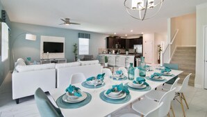 Un salon moderne avec un coin repas aménagé pour un repas, une cuisine en arrière-plan et un escalier menant à un autre niveau.