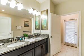 A bathroom with two sinks, a large mirror, and a door leading to another room. - 9073hs-the Retreat at Championsgate (Davenport)