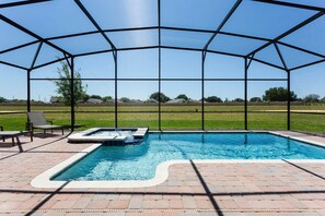 Una piscina scoperta coperta con una vasca idromassaggio, circondata da un patio in mattoni e vista su un prato.