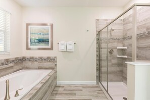 Um banheiro moderno com uma banheira grande, chuveiro com divisória de vidro e piso revestido com azulejos.