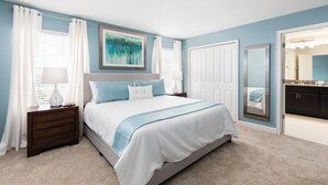 A bedroom with a bed, nightstands, a lamp, a painting, and a door leading to a bathroom. - 9077dd - NON Renting 2-15-21 the Retreat at Championsgate (Davenport)