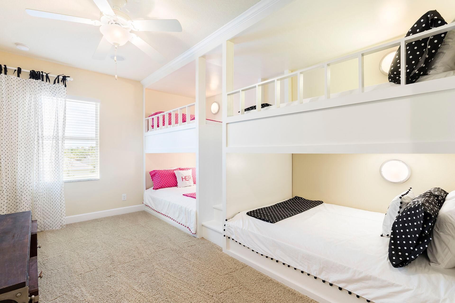 A bunk bed room with a ceiling fan, a window with curtains, and a small table.