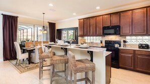 A modern kitchen with dark wood cabinets, a central island with bar stools, a black microwave, and a stove. - 4049otd-solterra Gated Resort (Davenport)