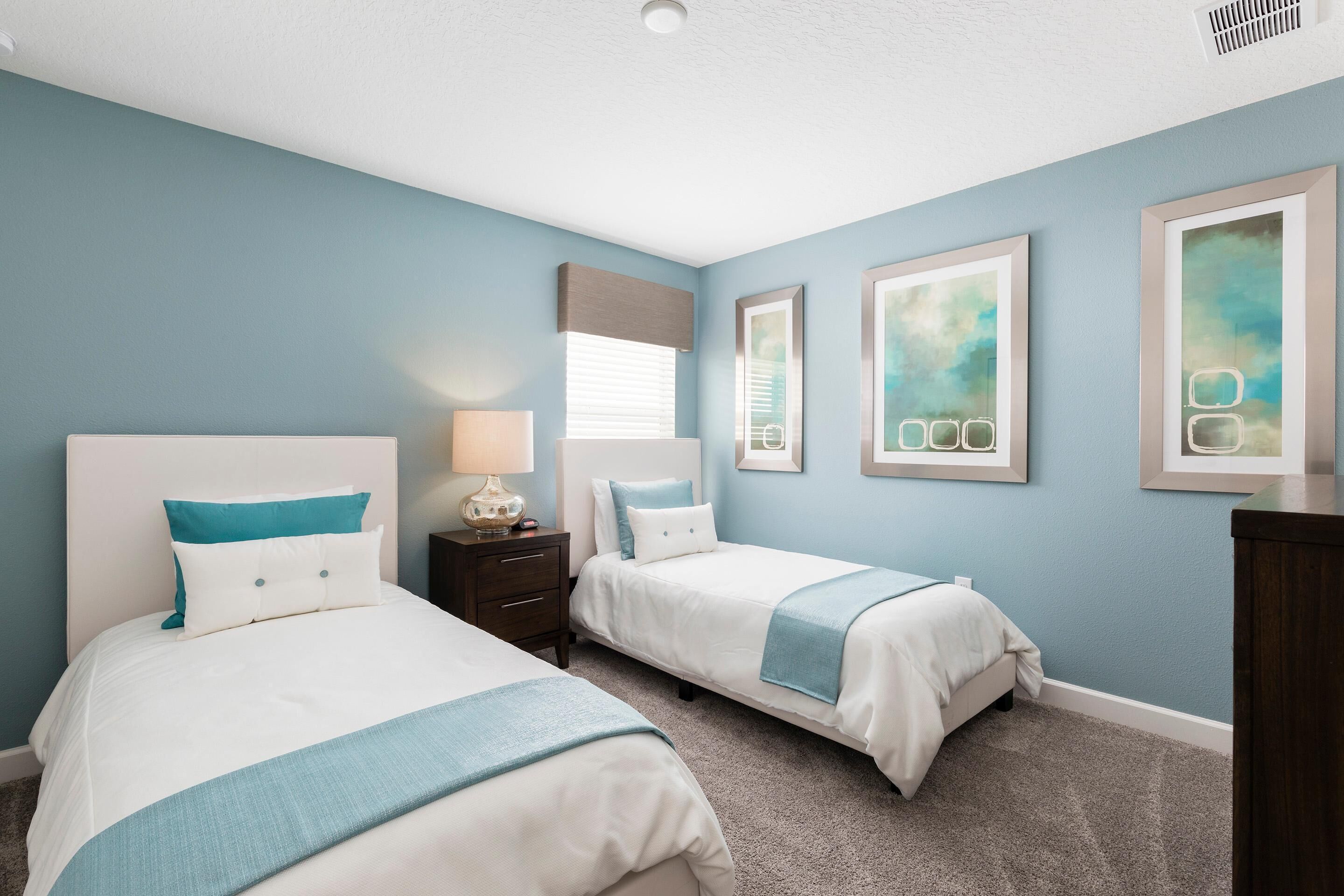 A bedroom with two beds, a nightstand, a lamp, and artwork on the walls.