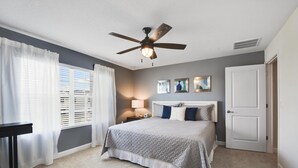 A bedroom with a bed, a ceiling fan, a nightstand with a lamp, and a door.